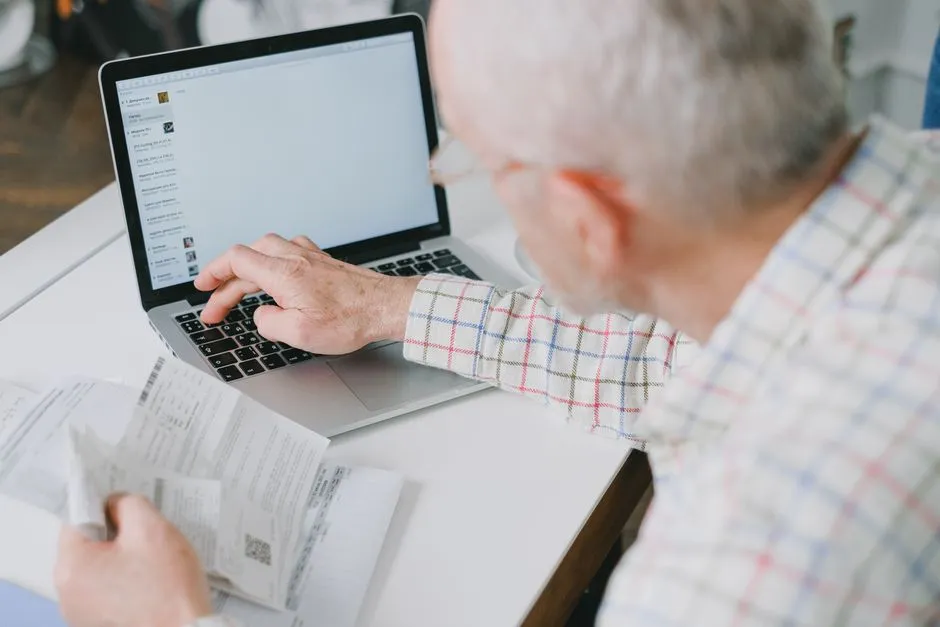 A person reviewing paperwork while typing on a laptop
